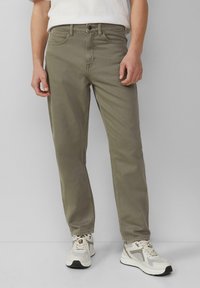 Oliwkowe bawełniane spodnie z prostymi nogawkami, pięcioma kieszeniami i zapięciem na guzik, połączone z jasnoszarymi butami sportowymi.