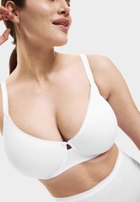 Sujetador blanco con tirantes ajustables, bordes ondulados y textura suave, diseño con cierre delantero.