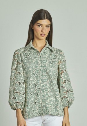 Spitzenbluse in sanftem Grün mit floralem Muster, Knopfverschluss vorn und Ballonärmeln mit elastischen Bündchen. Mit feinen Details versehen.