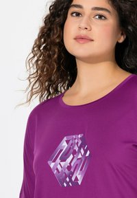 Paarse korte mouwen shirt met een hexagonaal grafisch patroon in tinten paars en wit op de borst. Zachte textuur en ronde halslijn.