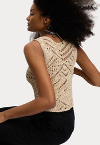 Beige pletený crop top s texturovaným otevřeným vzorem, s bezramenným střihem a uvolněným střihem, spárován s tmavými kalhotami.