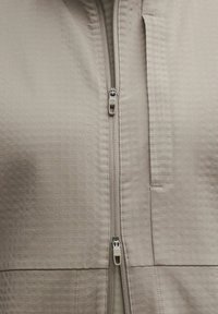 Bežna zip-up jakna z izvezenim vzorcem, pokončno ovratnico in zadrgo na žepu. Izdelana iz lahkega, zračnega materiala.