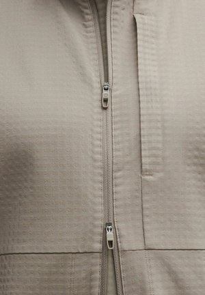 Chaqueta beige con cremallera que presenta un patrón texturizado, cuello alzado y un bolsillo con cremallera. Confeccionada con un material ligero y transpirable.