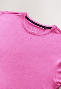 Maglietta sportiva rosa con scollo tondo e maniche corte. Presenta un tessuto strutturato e un'etichetta nera sul collo.