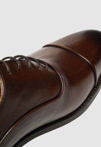 Scarpa da uomo in pelle marrone con punta arrotondata, dettagli lungo i lati e stringhe scure. La finitura è lucidada, evidenziando la sua superficie liscia.