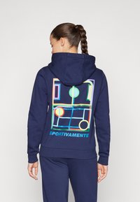 Navy mikina s živým geometrickým vzorom na chrbte, obsahujúcim kruhy a obdĺžniky. Text „SPORTIVAMENTE“ na spodnej strane. Zmes bavlny.