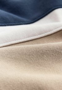 Textúrované tkaninové vrstvy v námorníckej, krémovej a béžovej farbe s hladkým povrchom. Výrazné švy pozdĺž okrajov a rôzne hrúbky.