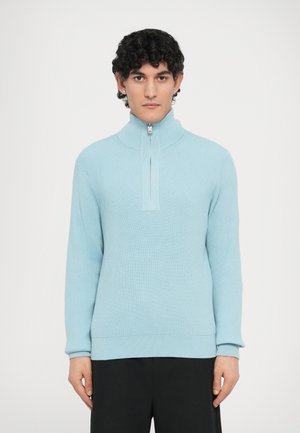 Pull bleu clair côtelé avec un col montant et une fermeture à demi-zip, doté de manches longues et d'une coupe décontractée. Texture lisse et design minimaliste.