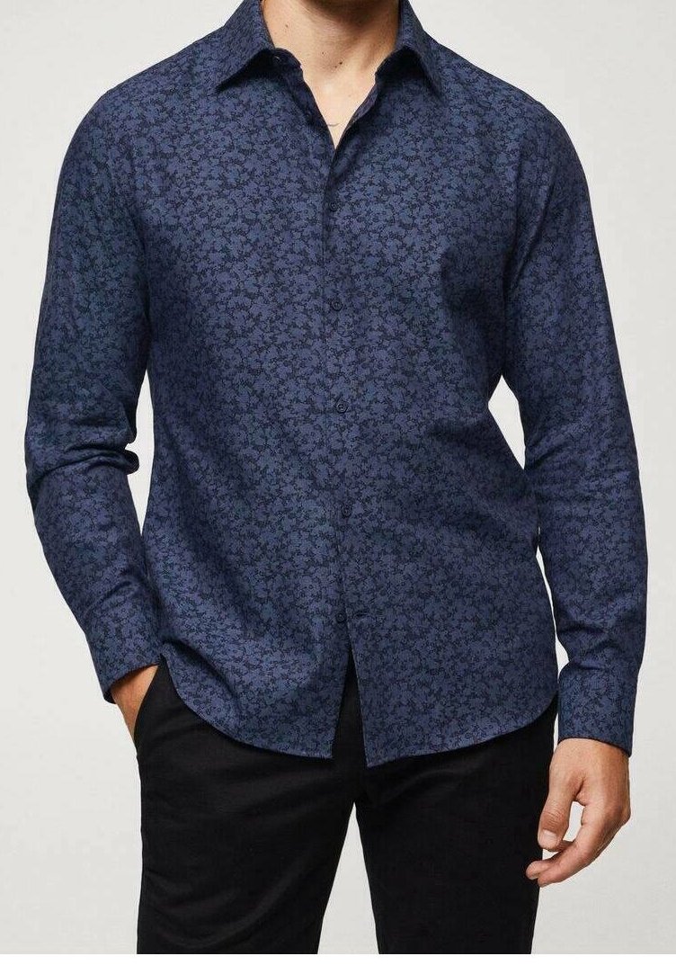 Homme portant une chemise à manches longues bleu foncé à motifs floraux avec un pantalon noir, debout avec une main dans la poche.