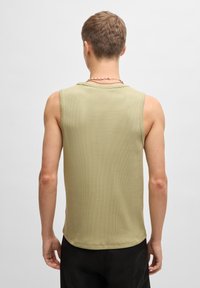 Débardeur sans manches vert olive clair en tissu texturé, avec un col rond et une coupe décontractée. Pas de motifs ou de quincailleries notables.