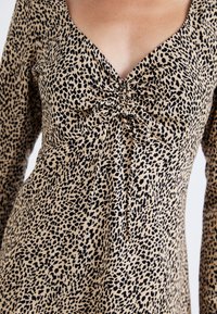 Μπλούζα με λεοπάρ σχέδιο σε μπεζ και μαύρο, με V λαιμόκοψη και ραφές στο στήθος, κατασκευασμένη από μαλακό, υφαντό ύφασμα.