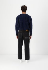 Marineblå struktureret sweater med abstrakt mønster parret med sorte jeans med kontrasterende syninger og broderet logo; hvide sneakers fuldender looket.