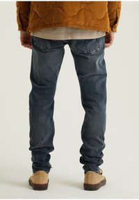 Mörkblå denimjeans med slim fit, fem fickor och lätt blekning. Kombinerat med beige, låga skor och en texturerad, senapsgul tröja.