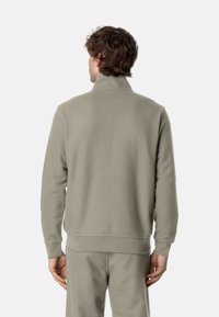 Felpa con zip grigia chiara, collo alto, polsini e fascia in maglia, realizzata in un tessuto morbido, vista da dietro.