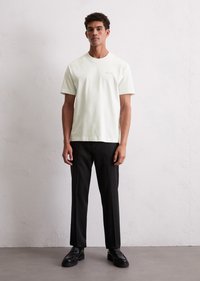 Light-colored, short-sleeve t-shirt with a crew neck, paired with black trousers and black shoes. Simple design with minimal branding detail.