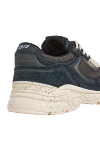 Sneaker con tomaia blu scuro, tessuto testurizzato, dettagli in rete e una suola spessa bianca sporca con macchie nere. Brand sulla parte posteriore.