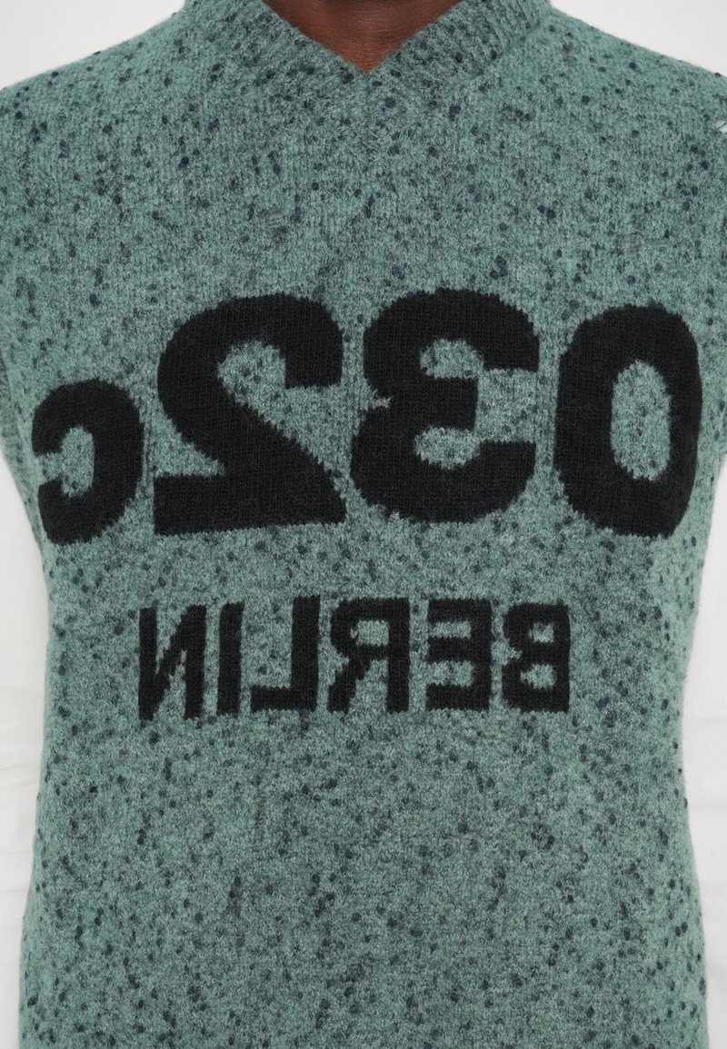 Gilet lavorato a maglia di colore verde con una texture marmorizzata. Presenta un grande testo nero con la scritta "032C BERLIN" in evidenza sulla parte anteriore.