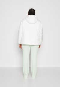 White padded jacket with a hood, featuring a quilted design. Paired with light green ribbed knit pants. Back view shows overall fit.