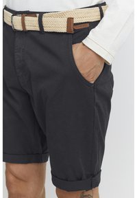 Shorts en coton noir avec ourlets roulés, dotés de poches latérales, associés à une ceinture tissée beige et à un accent en cuir.