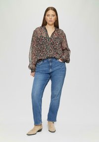 Schwarze Bluse mit floralem Muster, puffartigen Ärmeln und tiefem V-Ausschnitt, kombiniert mit hellblauen Jeans und beigen Stiefeletten. Weicher, fließender Stofftextur.