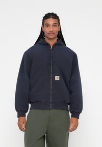Marineblå zip-up hættetrøje lavet af en bomuldsblanding, der har en kengurulomme, ribbede manchetter og kant, samt et lille logo-patch på forsiden.