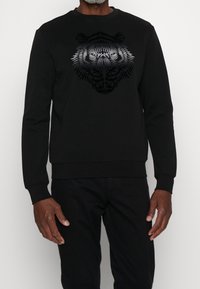 Sudadera negra con un gráfico de tigre en tonos de gris, fabricada con material suave, de cuello redondo y con puños y dobladillo acanalados.