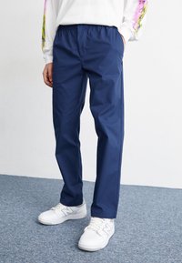 Pantaloni elasticizzati blu navy realizzati in tessuto leggero, con una vestibilità a gamba dritta e indossati con sneakers bianche.