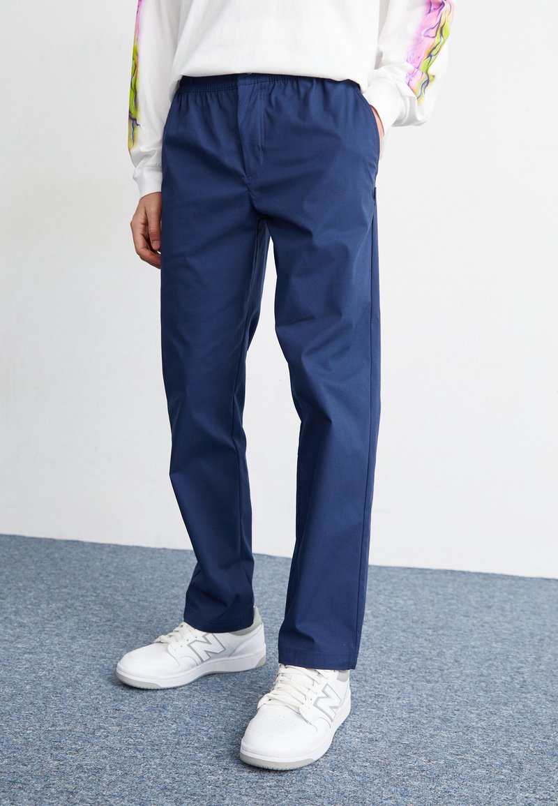 Pantaloni elasticizzati blu navy realizzati in tessuto leggero, con una vestibilità a gamba dritta e indossati con sneakers bianche.