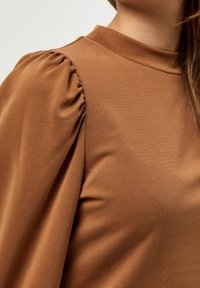 Brun långärmad tröja med hög halsringning, rynkade puffärmar och ett mjukt, texturerat material.