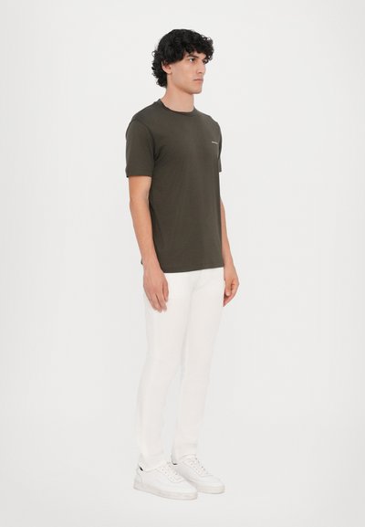 T-shirt en coton vert olive à manches courtes, col rond et poche sur la poitrine gauche, associé à un pantalon blanc ajusté et des baskets blanches.