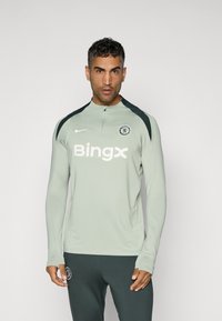 Hellgrünes langärmliges Trainingstop mit schwarzen Akzenten, hoher Kragen, Chelsea FC-Logo und dem weißen Text "Bingx" auf der Brust.