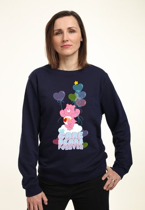 Marineblå sweatshirt med et stort Care Bears grafik, der viser en pink bjørn, der holder farverige balloner, prydet med hjerter og et stjernemotiv.