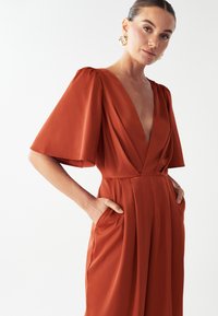 Vestido de color óxido hecho de una tela suave, con mangas cortas y anchas, un escote en V profundo y bolsillos laterales, con un corte holgado.