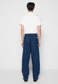 Biały krótki rękaw koszulki polo w połączeniu z luźnymi, ciemnoniebieskimi spodniami jeansowymi, posiadającymi elastyczny pas i tylnią kieszeń.