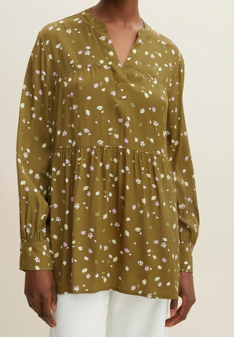 Blouse vert olive avec un col en V, manches longues et taille froncée. Présente un motif floral en blanc, rose et vert. Texture de tissu doux.