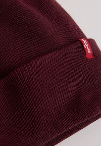 Bordeaux beanie gemaakt van geribbeld breimateriaal, met een opgerolde zoom en een klein rood Levi's label aan de zijkant.