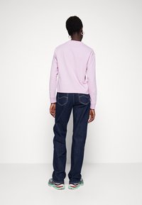 Top de manga larga color púrpura claro con escote redondo, combinado con jeans de mezclilla azul oscuro que cuentan con bolsillos traseros y un corte recto.