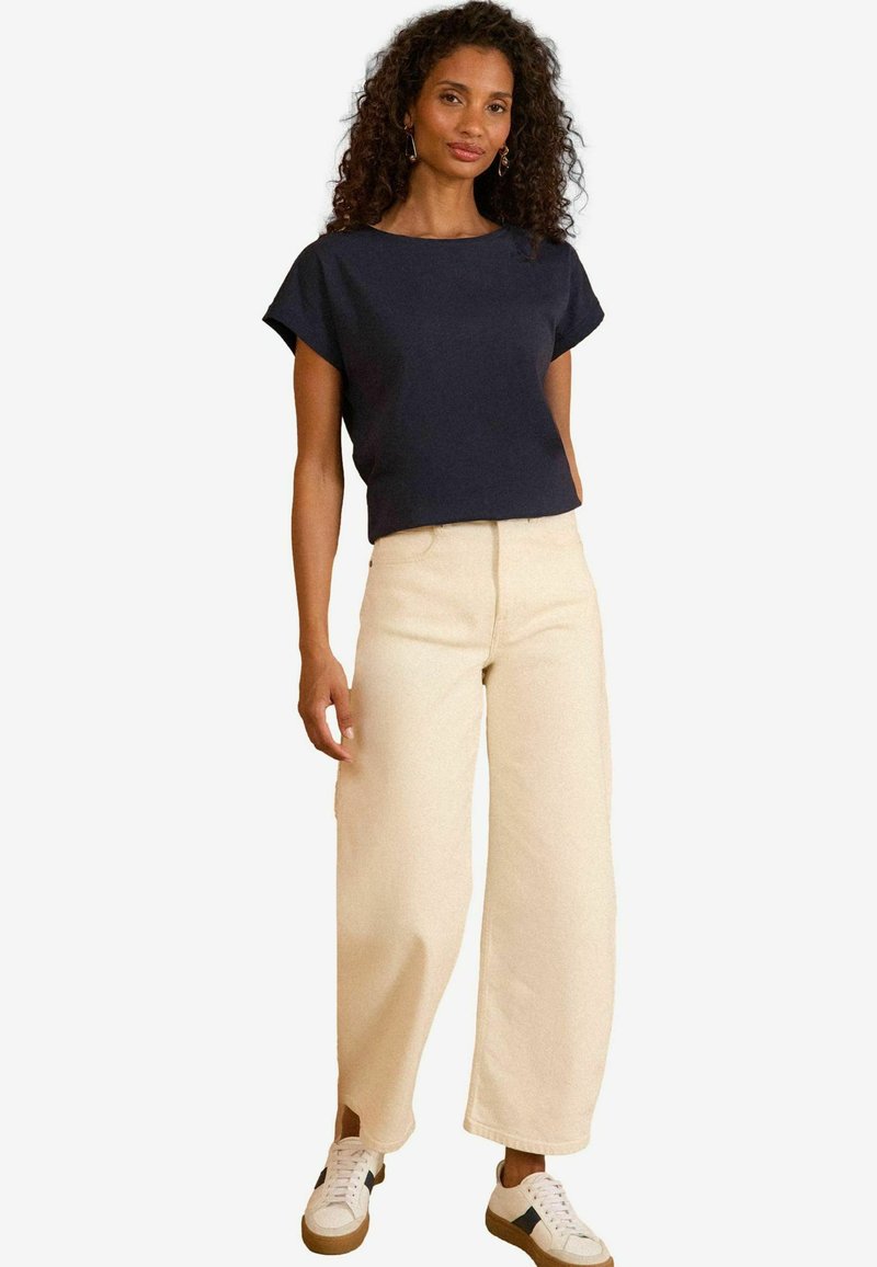Top corto navy a maniche corte abbinato a pantaloni larghi color crema e sneaker bianche con accenti scuri. Tessuto morbido, design casual.