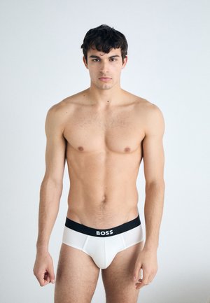 Boxeri albi cu un elastic negru pe care este inscripționat logo-ul "BOSS", confecționați dintr-un material neted, cu un design ajustat și o croială clasică, prezentati pe un model.