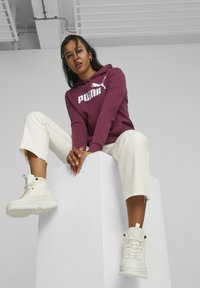 Maroon hoodie with white Puma logo, cream wide-leg pants with frayed hem, and white high-top sneakers, positioned on a white pedestal.