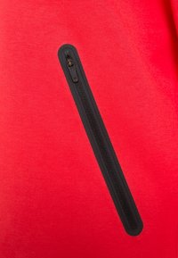 Red fleece fabric featuring a vertical black zippered pocket with a smooth, textured zipper. Simple, functional design detail.