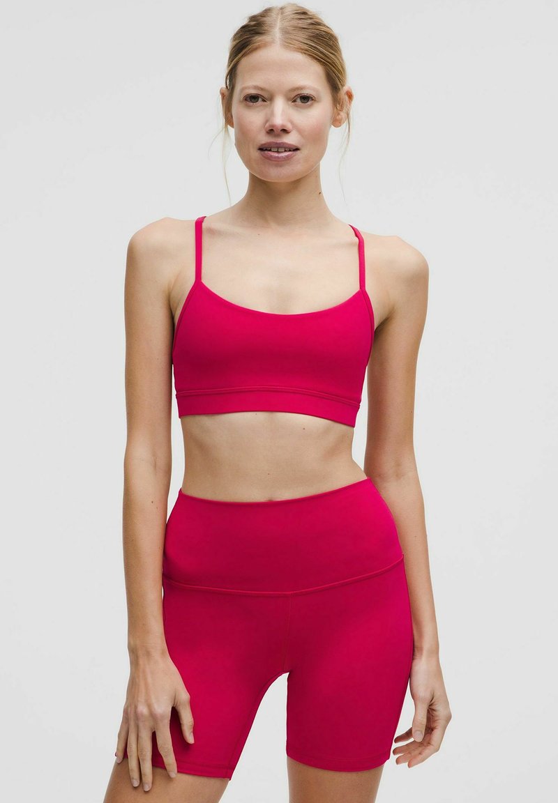 Dopasowany zestaw sportowy w jaskrawym różu. Top ma cienkie ramiączka; szorty z wysokim stanem wykonane są z gładkiego, elastycznego materiału.