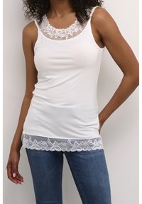 Top blanco sin mangas con encaje en el escote y el dobladillo inferior; presenta un diseño ajustado y una textura de algodón suave. Combinado con jeans azules.