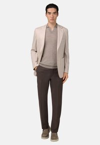 Blazer beige clair, pull en V marron clair, pantalon ajusté marron foncé et chaussures décontractées grises. Tissu lisse et design structuré.