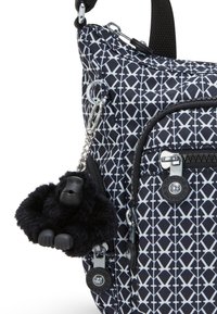 Sort-hvid mønstrede crossbody taske med tekstureret stof, lynlåse og en sort fluffy gorilla nøglekæde vedhæftet.