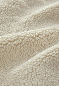 Gros plan d'un tissu texturé doux de couleur crème avec une surface bouclée et moelleuse et des plis doux créant des ombres.
