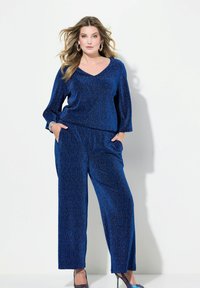 Completo due pezzi metallici blu composto da un top a V con maniche lunghe e pantaloni a gamba larga. Tessuto morbido con un sottile effetto scintillante.