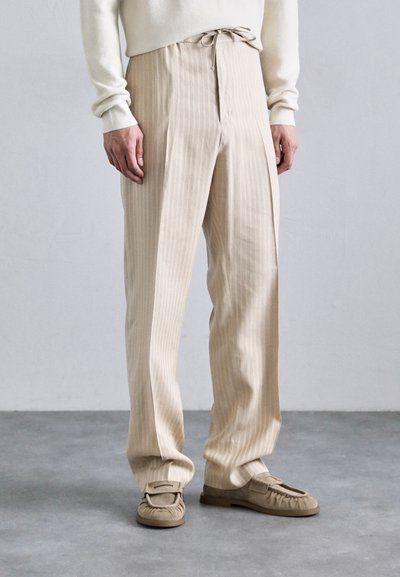Pantaloni beige a righe con una vestibilità rilassata, dotati di una cintura in vita e pieghe laterali. Abbinati a mocassini leggeri in suede.