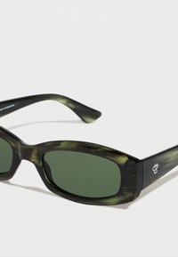 Πράσινα γυαλιά ηλίου με ελαφρύ, ελαφρώς διαφανές μαύρο και πράσινο σκελετό. Διαθέτουν ορθογώνιο σχήμα και διακριτική σήμανση στο στέλεχος.