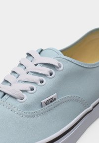 Baskets Vans bleu clair avec lacets blancs, semelle en caoutchouc blanche et étiquette logo Vans visible sur la tige en tissu.